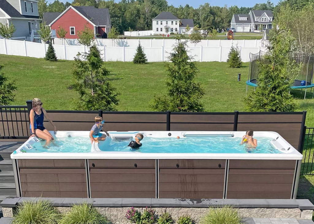 A smiling family enjoys their swim spa in a backyard space with green grass in the background.