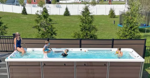 A smiling family enjoys their swim spa in a backyard space with green grass in the background.