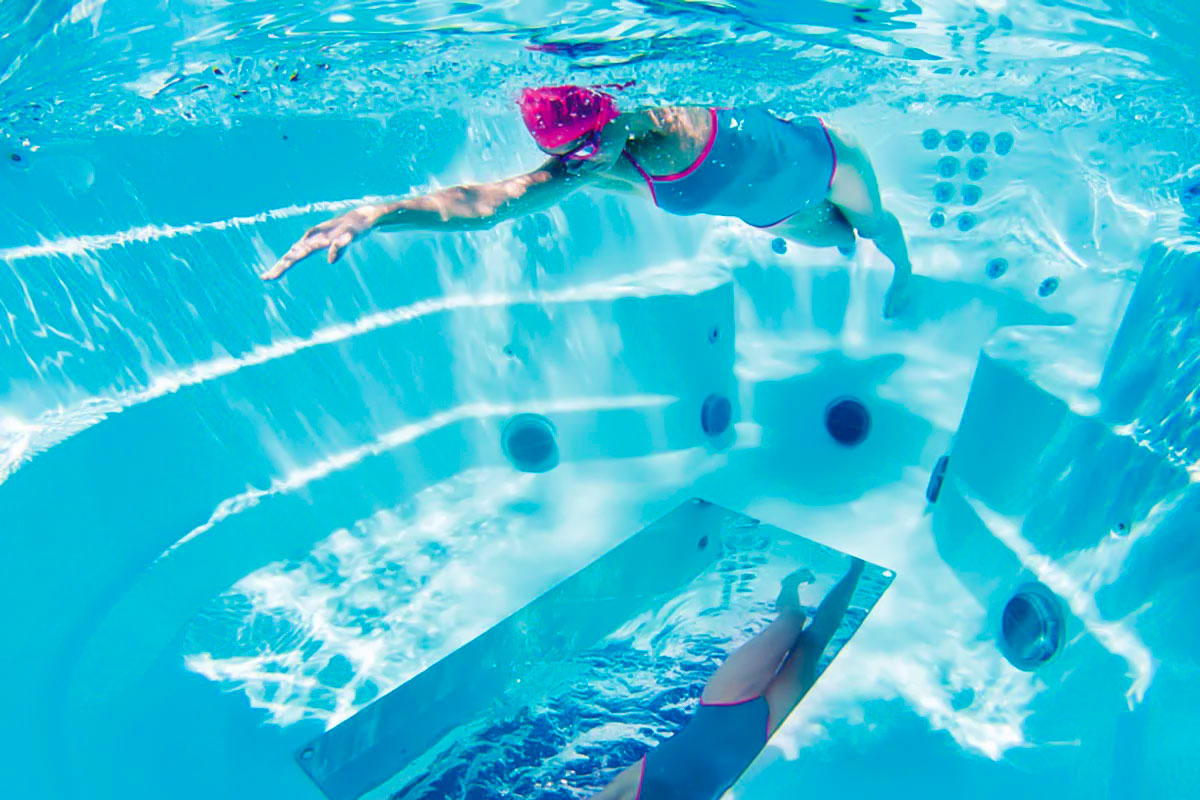 a woman practices her swim technique using the built in floor mirror of her swim spa