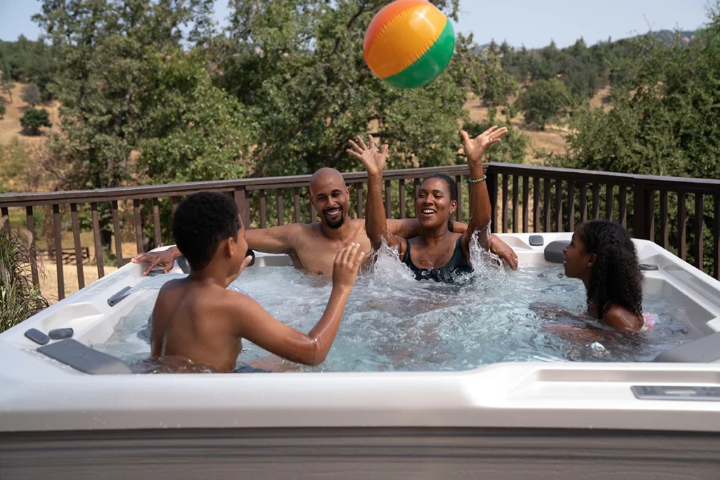 A family of four plays a game with an inflatable ball outdoors in a HotSpot hot tub.