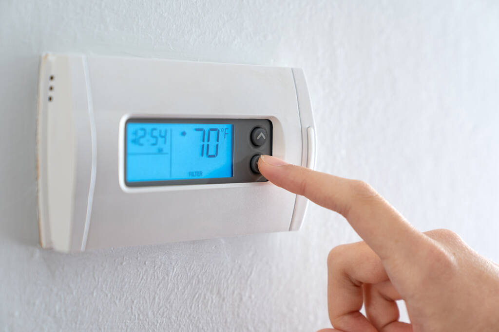 A hand adjusting a thermostat against a white wall