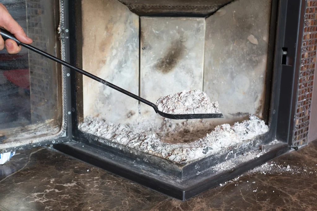 A hand holding a shovel, cleaning ashes from a fireplace