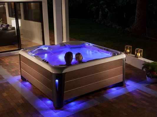 Couple soaking in a HotSpring Highlife at night with multi color LED lights illuminating the water and the surrounding deck