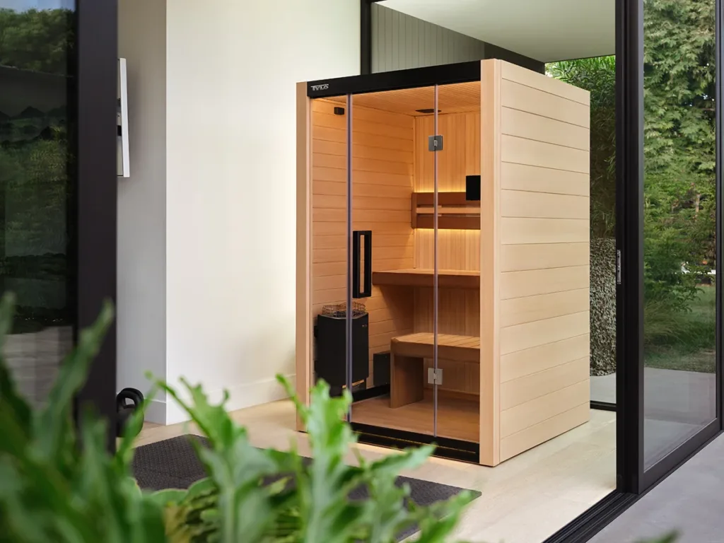 An indoor wooden infrared sauna, in a bright room with indoor plants