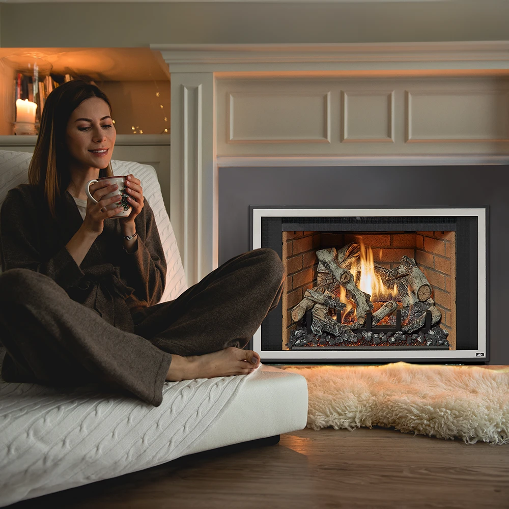 A happy women sitting on a couch holding a mug of coffee, enjoying the warmth of a Lopi 430 Deluxe Gas Fireplace Insert