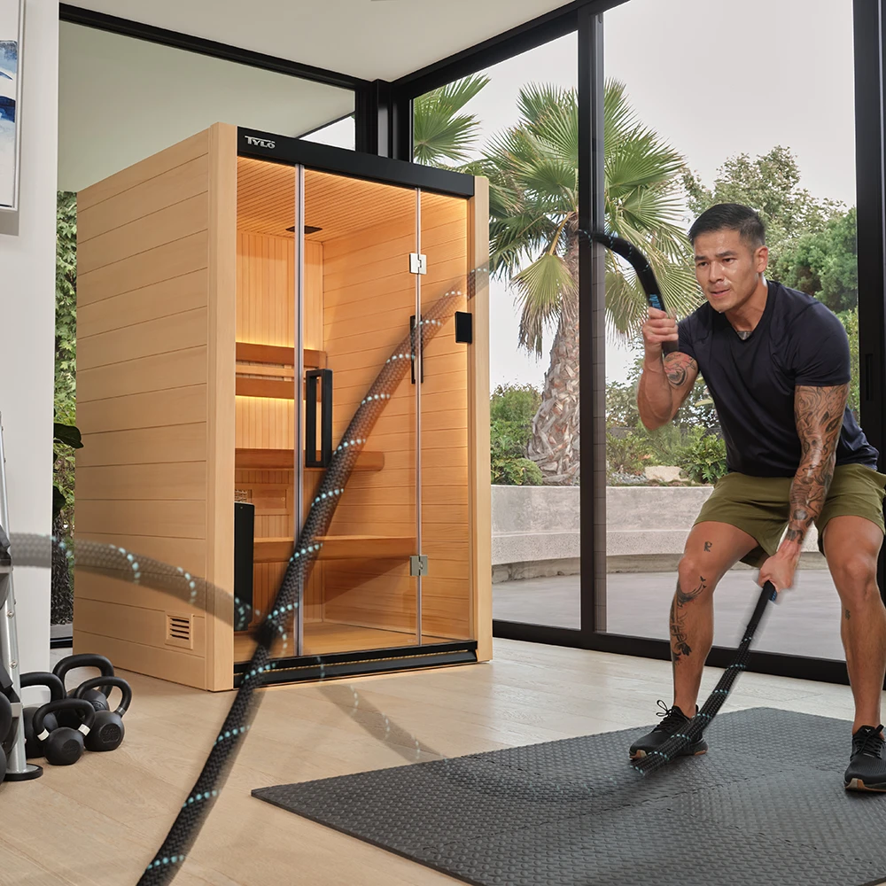 A man exercising in home gym, with a Tylö HALMSTAD 2 sauna in the background 